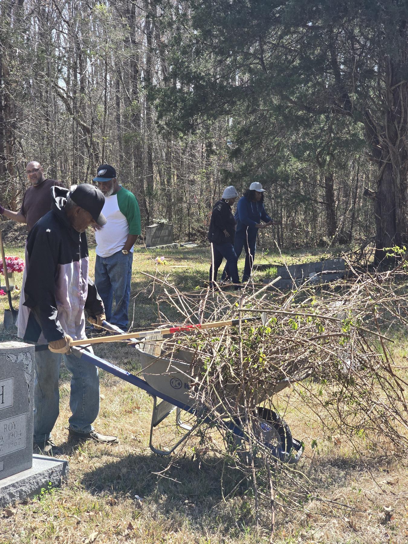 Volunteers clearing brush and debris with a wheelbarrow at Snow Hill Cemetery