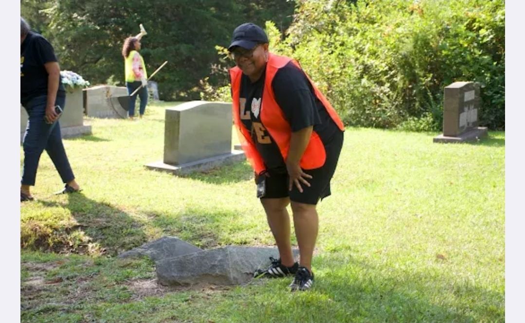 Volunteer in orange safety vest standing near a reset headstone at Snow Hill Cemetery