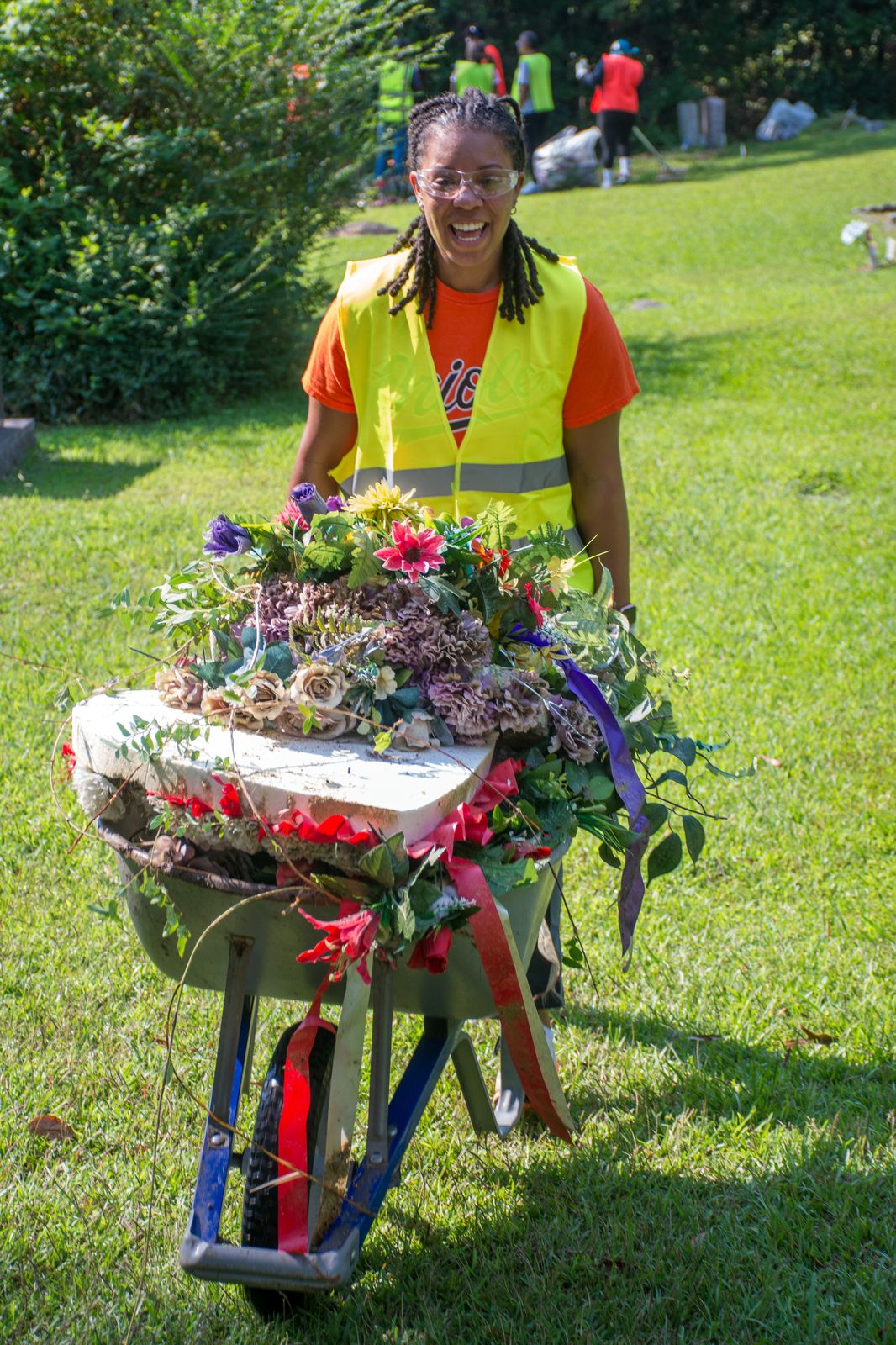 Volunteer smiling while pushing a wheelbarrow filled with flowers during cemetery clean-up