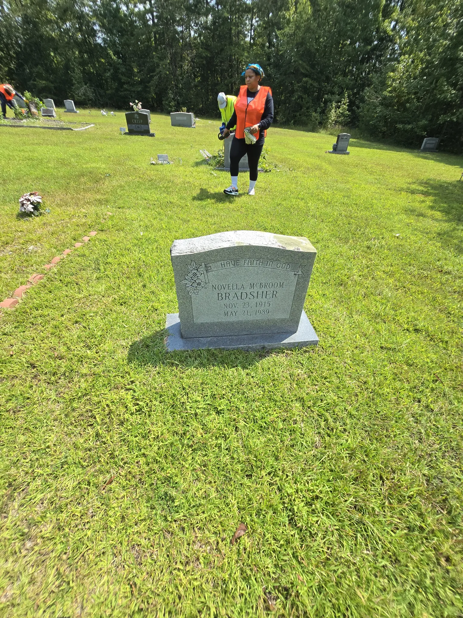 Volunteer in orange safety vest standing in front of Bradsher family headstone